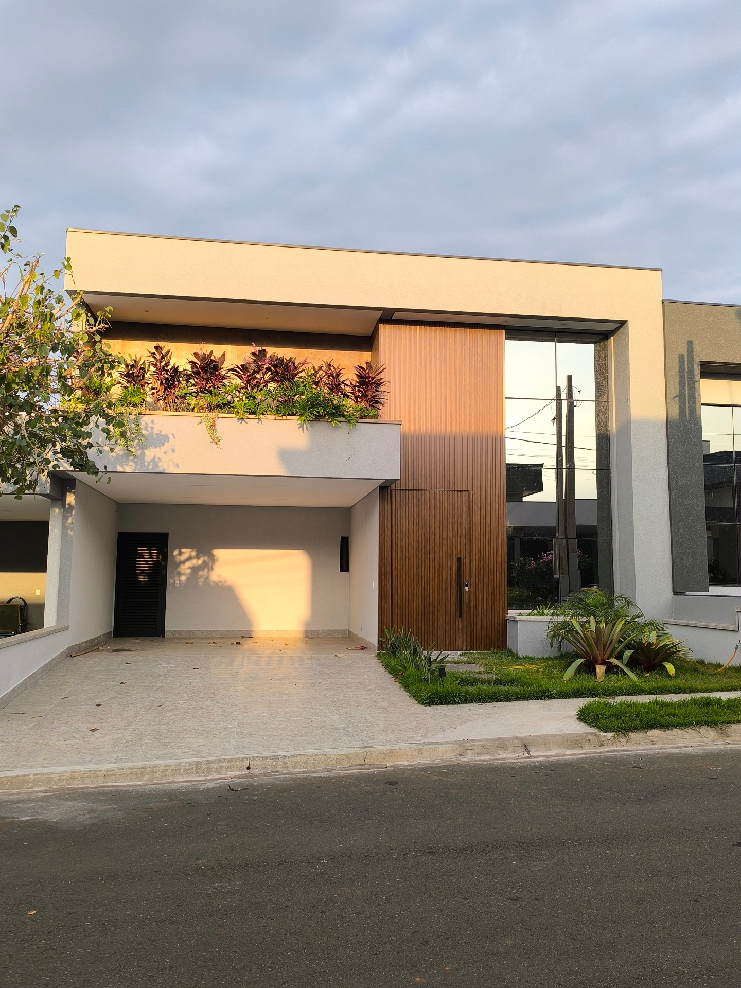 Fachada moderna com porta pivotante em madeira e esquadrias amplas